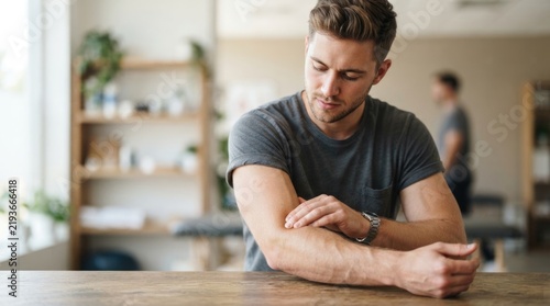 Concerned Young Man Touching Sore Elbow and Examining Arm for Pain or Injury at Home