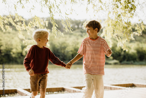 Two joyful boys exploring nature by the lake, hand in hand, on a sunny day