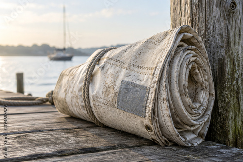 Weathered sailcloth with stitching, rolled against a wooden dock post.