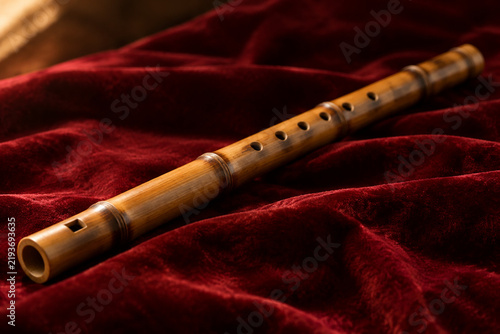 A bamboo flute rests on deep red velvet, side lighting.