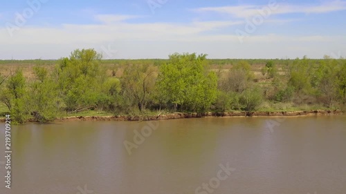 Scenic view of the muddy Parana River in Argentina flowing past green grassy banks and lush trees under a bright blue sky with light clouds, showcasing serene wild natural South American landscape