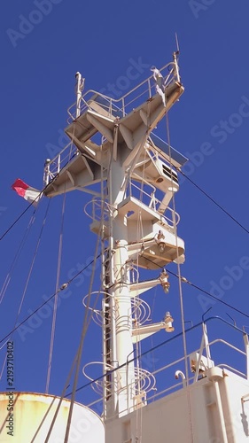 Tall steel radar mast of a vessel equipped with communication antennas, riggings, and navigation equipment against a clear blue sky, capturing maritime technology and marine transport