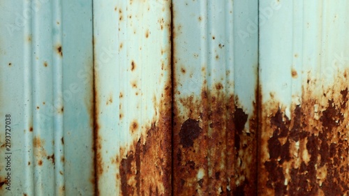 Close-up texture of vertical corrugated metal panels covered in flaking turquoise paint and dark rusty corrosion.