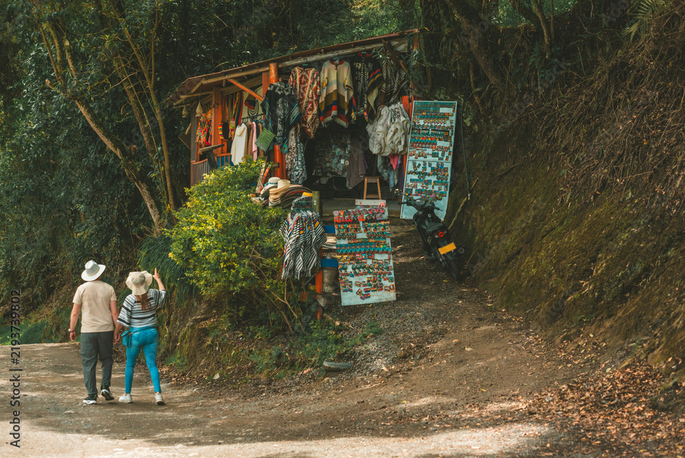 Fototapeta premium Hikers walking along a forest trail beside a small roadside souvenir stall, combining outdoor adventure, tourism and local commerce.