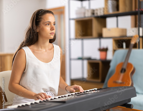 Fotografía Young woman wears shorts, sits at synthesizer and plays music in room