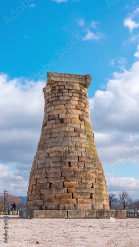 Vertical time lapse of Cheomseongdae ancient observatory in Gyeongju, South Korea, with moving clouds and changing daylight against a bright blue sky.