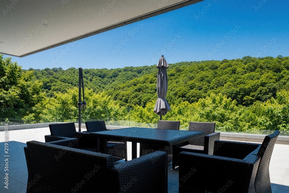 Fototapeta premium Modern dark rattan patio set with table and chairs overlooks lush green forest hills. This outdoor living space offers comfortable seating and a relaxing view under a bright blue sky.