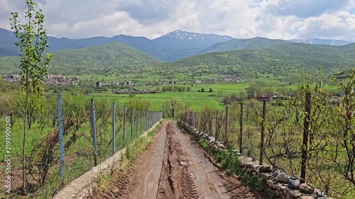 Rustic dirt road stretches toward snow-streaked mountains, lined by young orchards, a stone wall, and rolling green hills beneath dramatic clouds.
📍 Dorud, Sarvabad, Kurdistan 