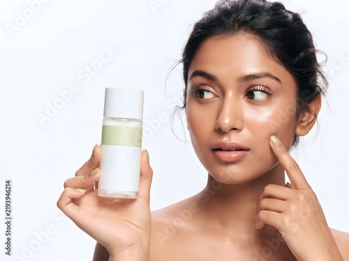 Woman Applying Skincare Product While Holding Cosmetic Bottle