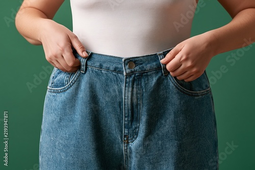Person struggling to button tight jeans on green