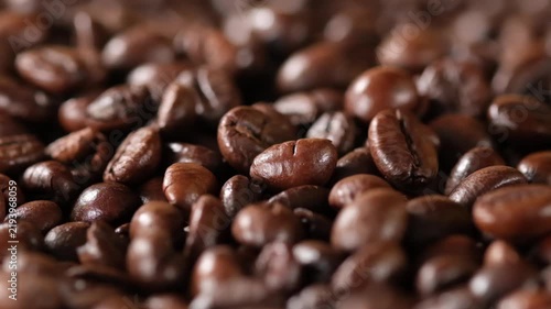 Extreme close-up of roasted coffee beans falling from above, highlighting the different shapes, sizes and textures of the beans as they land.