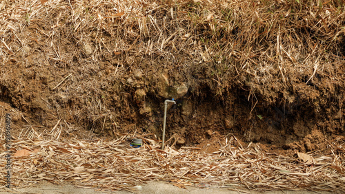Canvastavla A view of a hollowed-out earthen slope featuring a water pipe and an outdoor tap installed on an earthen embankment covered with dry bamboo leaves