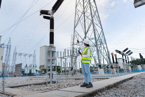 Fotografie Outdoor switchyard pylon inspection shows the transmission tower and disconnect switch while a technician points at the tower with a tablet