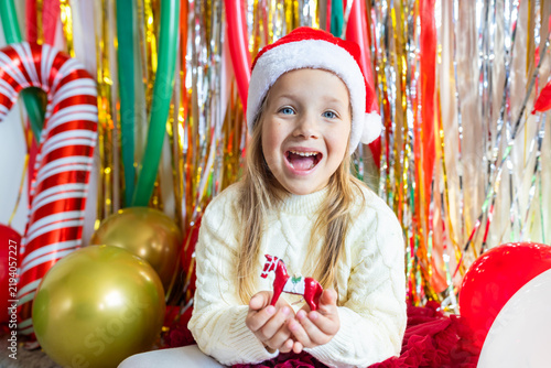 Smiling young girl in Santa hat holding red toy horse at festive background