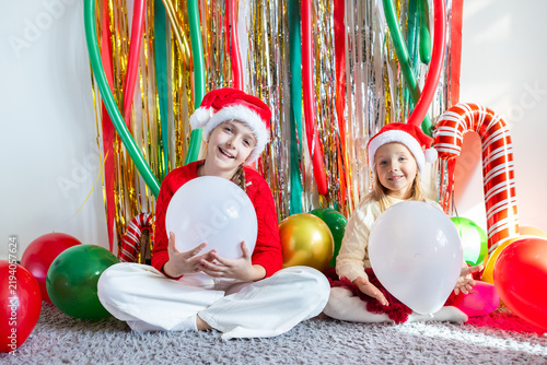 Smiling girls wearing Santa hats holding balloons during festive celebration