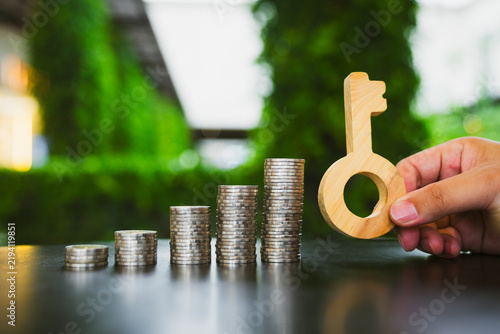 Fotografía Real estate investment and financial success concept, hand holding wooden key beside ascending stacks of coins on table, symbolizing home loan, property purchase, and mortgage growth