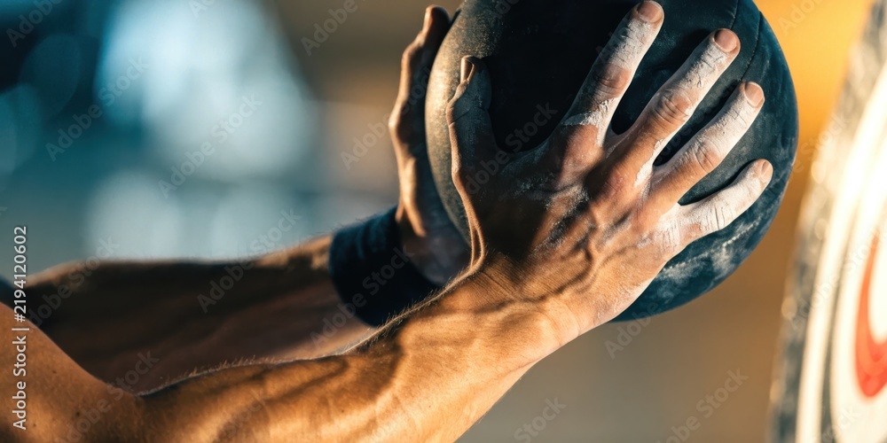 Obraz premium hyrox workout race concept. Close-up of muscular hands gripping a heavy medicine ball during an intense workout session.