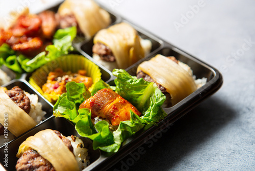 Gourmet Korean bento box featuring spicy stir-fried pork, beef bulgogi, and rice wrapped in kimchi and lettuce