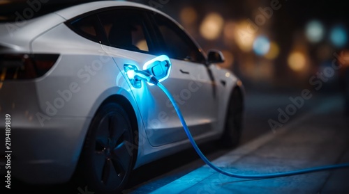 Modern white electric car at night showcasing glowing blue charging cable, illuminated power port and sleek vehicle body, representing sustainable transportation and clean energy technology