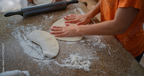 Hands pressing raw dough flat on a flour covered kitchen countertop