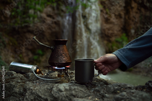 Foto Outdoor coffee ritual with a titanium cup and Turkish coffee pot prepared on a portable camping stove near a waterfall