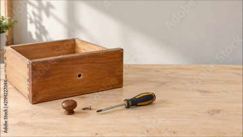 Wooden drawer with screwdriver and loose knob on workbench for furniture repair with copy space