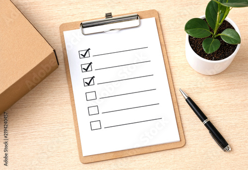 Checklist on clipboard with pen and small potted plant nearby