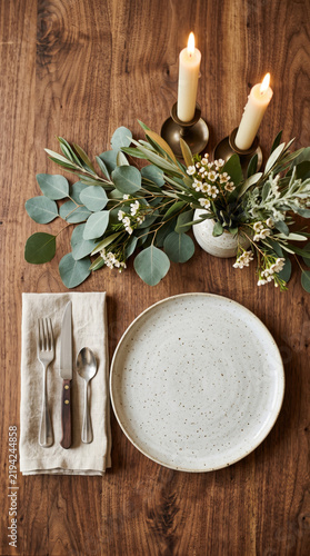 Minimalist top view of a dinner table setting with white candles and eucalyptus greenery on dark wood