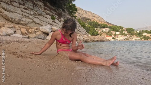 Girl playing with sand on a Croatian beach beside calm sea