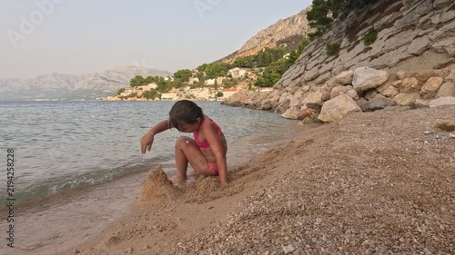 Girl playing with sand on a Croatian pebble beach by sea