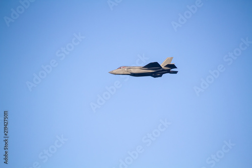 F-35A Lightning II fighter aircraft flying across a blue sky, photographed in side profile showing its distinctive stealth aircraft design.