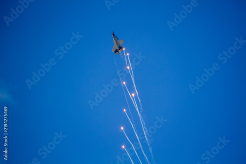 F-35A Lightning II fighter aircraft flying across a blue sky with visible vapor trails and clouds below, photographed in side profile showing its distinctive stealth aircraft design.