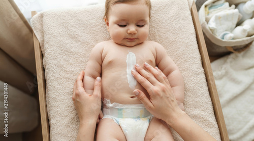 Adult hands applying protective cream on a cute infant's tummy, promoting delicate skincare, health, and a tender connection during daily baby care routine