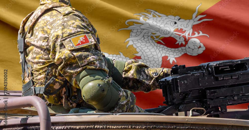 Obraz premium Bhutan flag with soldier at machine gun turret in front of it. Closeup side view.