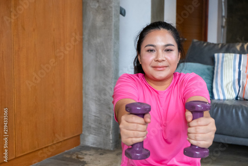 Fat woman holding purple dumbbell during exercise at home with calm focus and healthy lifestyle energy