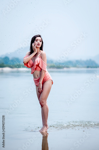 Joyful Asian woman cooling off in natural water splash during summer vacation, enjoying refreshed freedom.