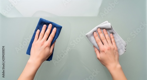 Person wiping a glass surface with two microfiber cloths from above