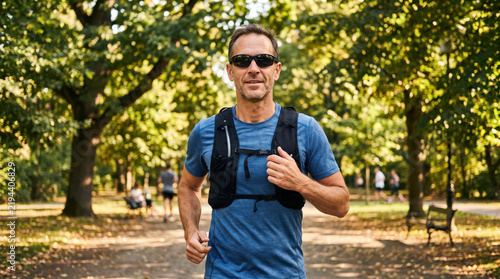 Middle aged man running in a park wearing a chest fitness monitor for outdoor training and health tracking concept