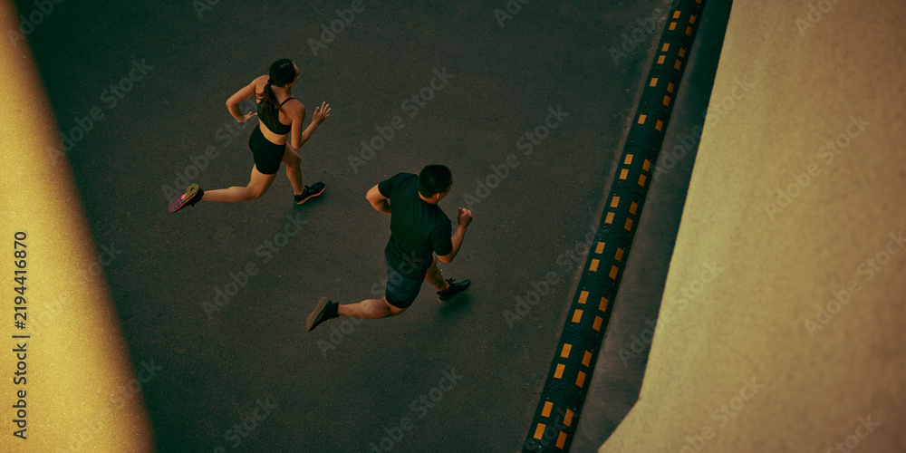 Fototapeta premium Fit young couple runs side by side along an urban route with powerful momentum. Outdoor training, cardiovascular health and shared goals concept.