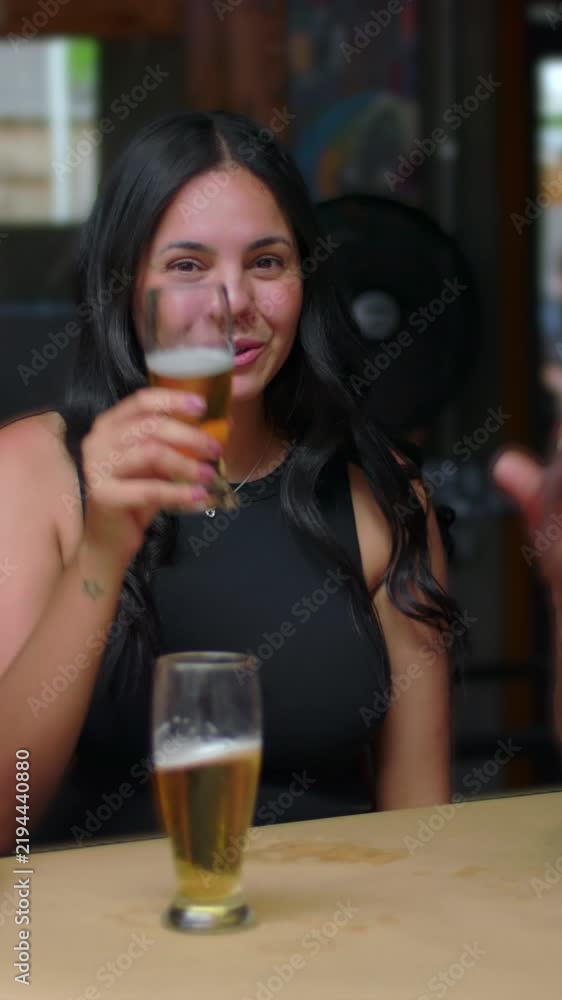 Smiling young women beckoning camera to join beer drinks at restaurant ...