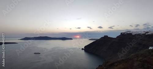 Fotografie Sunset view of the Santorini caldera with volcanic islands and calm Aegean Sea under warm evening light
