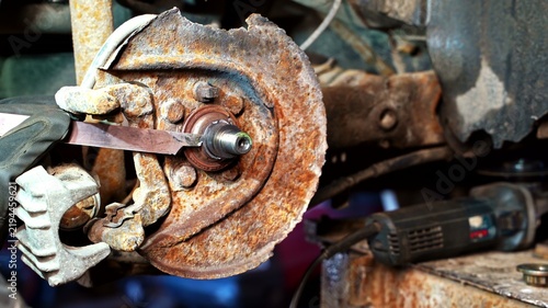 View of a mechanic using a tool on a heavily rusted car brake rotor and hub assembly in a workshop in Latvia.