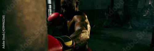 Fotografie Powerful boxer strikes a heavy bag in a dark industrial gym with fierce determination