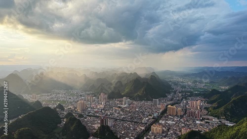 Urban scene: Rain shaft falling from dark clouds over a mountain city surrounded by karst peaks