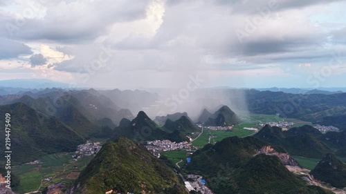 Landscape view: Rain shaft falling from dark clouds over karst mountains and rural villages