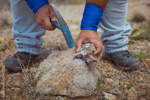 Quadro su tela Low angle action shot of a geologist or researcher using a rock pick hammer to break open a mineral sample outdoor on arid terrain during field work