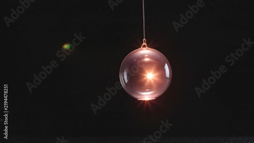 Cinematic video of a transparent hanging glass sphere illuminated by warm light with reflections against a deep black background.