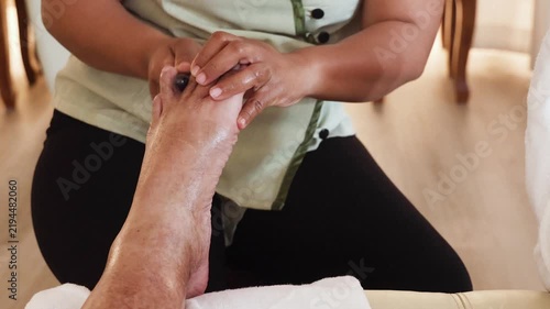 Close-up perspective view of masseuse using massage stick on toes in traditional relaxing and therapeutic Thai foot and leg massage, pressing on all essential acupoints.