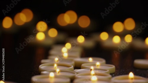 Lit candles flicker on a dark surface with warm defocused candlelight in the background. Memorial and remembrance media, meditation and mindfulness content, and wellness advertising.