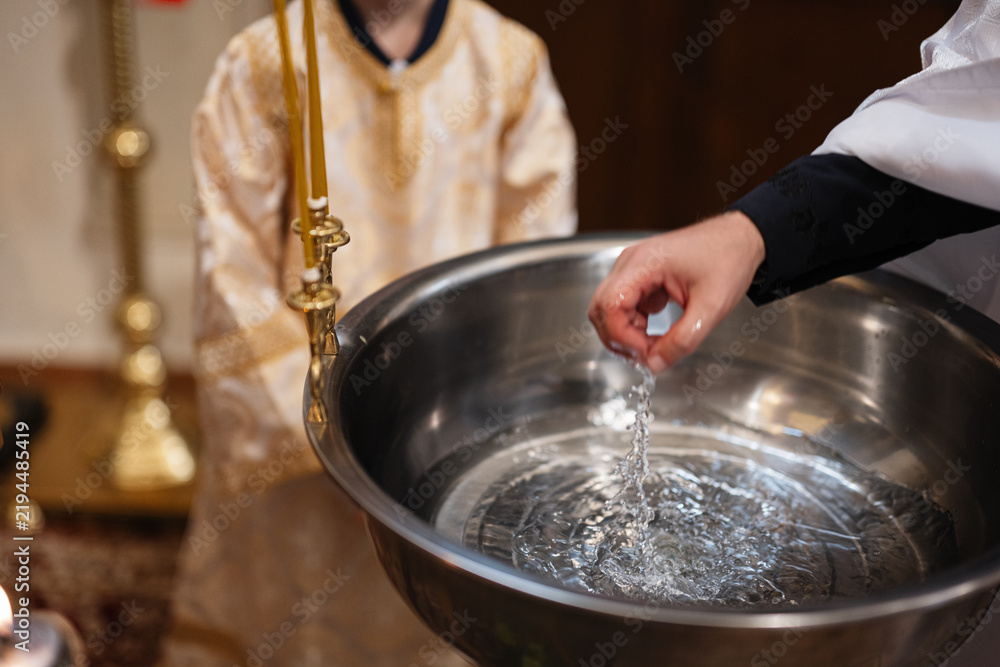 Fototapeta premium Priest pouring holy water from a baptismal font during a child christening ceremony in church